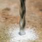 Drill bit penetrating a surface with water splashing around it.