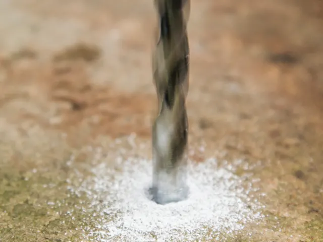 Drill bit penetrating a surface with water splashing around it.