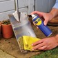 Person cleaning a rusty metal shovel with a yellow cloth and WD-40 spray.