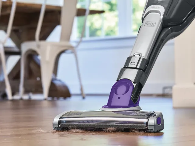 Vacuum cleaner cleaning a wooden floor in a room with furniture.