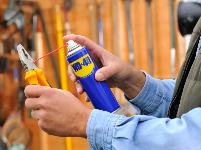 Person holding a can of WD-40 near pliers with a blurred tool chest background