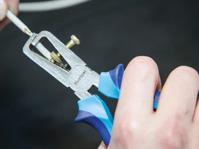 Close-up of a person using a blue and silver tool on a dark background