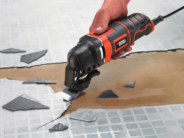 Person using a Black & Decker oscillating tool to cut tiles on a tiled floor.