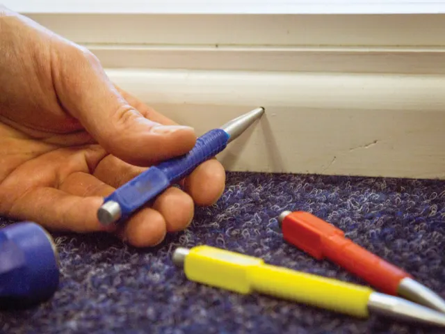 Hand holding a blue and silver pen next to other colorful pens on a textured surface.
