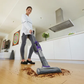 Person using a vacuum cleaner on a wooden floor in a modern kitchen.