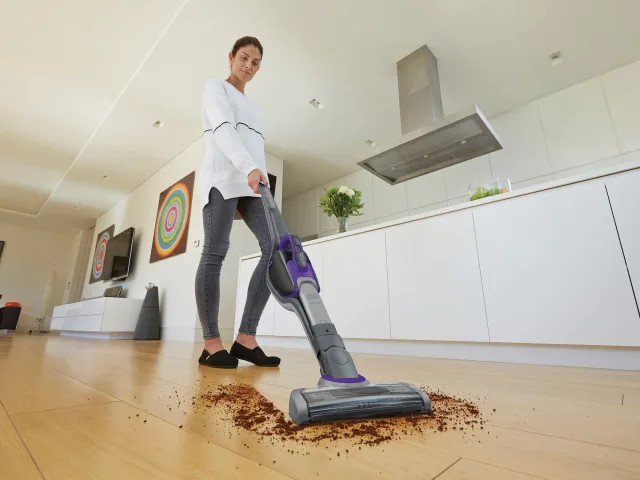 Person using a vacuum cleaner on a wooden floor in a modern kitchen.