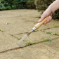 Person using a garden tool to remove weeds from concrete pavement