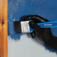 Hand wearing a black glove holding a BlueSpot paintbrush against a blue surface.