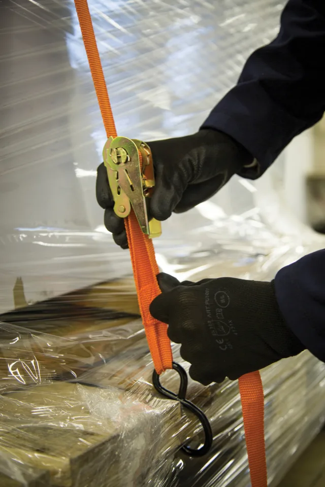 Person using an orange ratchet strap on a wrapped package