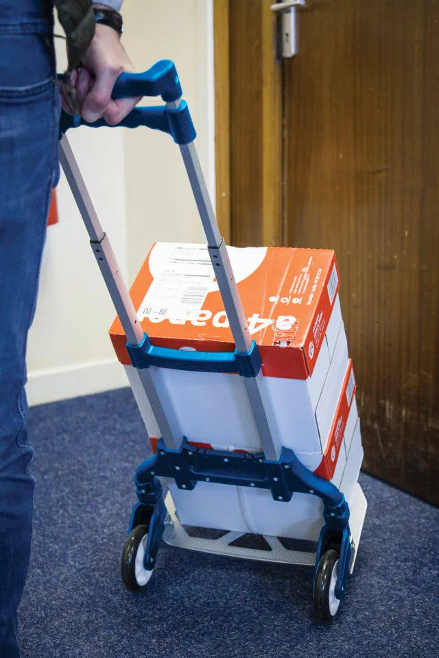 Person using a blue hand truck to move a box with Coca-Cola branding.