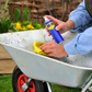 Person cleaning a wheelbarrow with a spray bottle and yellow cloth outdoors.