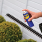 Person using a spray can labeled 'W240' on a hedge trimmer against a white wall.
