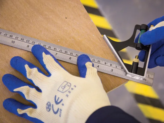 Person measuring wood with a ruler and wearing gloves