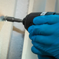 Person using a drill with a blue glove on a wooden surface