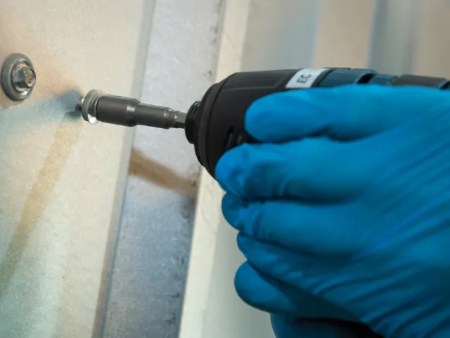Person using a drill with a blue glove on a wooden surface
