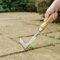 Hand using a lawn edger tool on a concrete surface with grass.