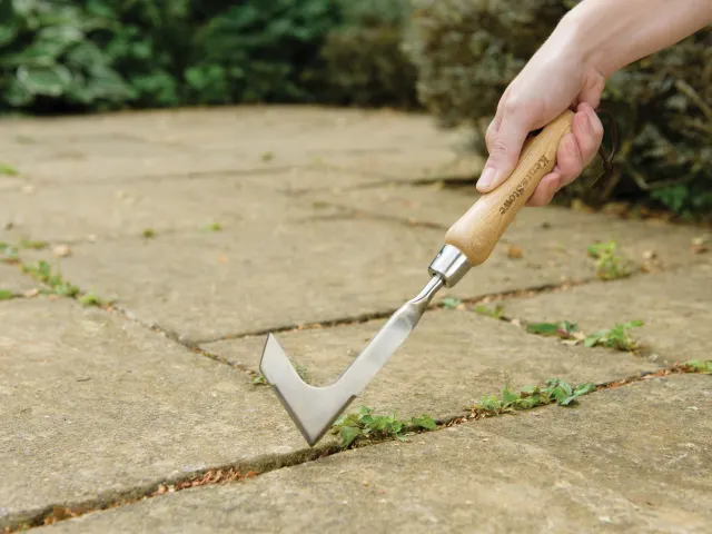 Hand using a lawn edger tool on a concrete surface with grass.