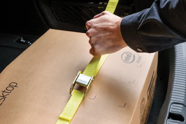 Person securing a cardboard box with a yellow strap inside a vehicle.