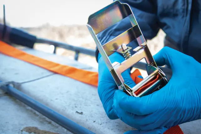 Person wearing blue gloves holding a reflective metal object with a blurred outdoor background