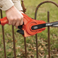 Person using a Black & Decker hedge trimmer on a rusty metal fence with grass in the background