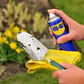 Person cleaning a garden trowel with a yellow cloth and WD-40 spray, outdoors.