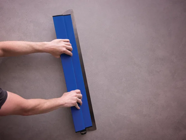 Person using a blue tool on a gray surface