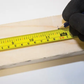 Hand holding a yellow measuring tape on a wooden surface