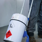 Person pushing a white hazardous materials container with blue handles.