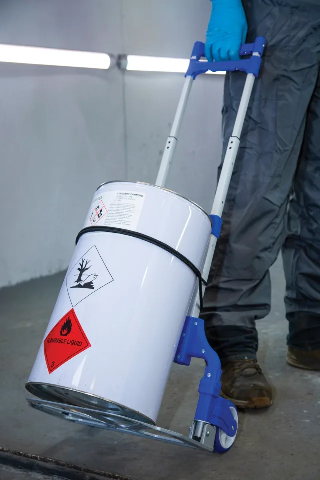 Person pushing a white hazardous materials container with blue handles.