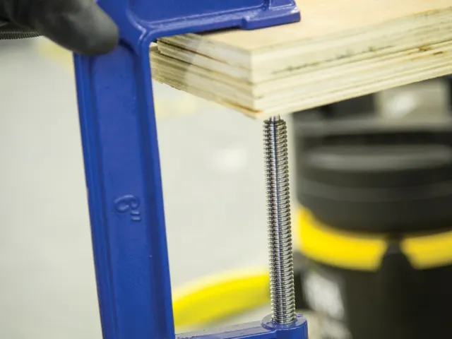 Blue vise holding a piece of wood on a workbench with a blurred background