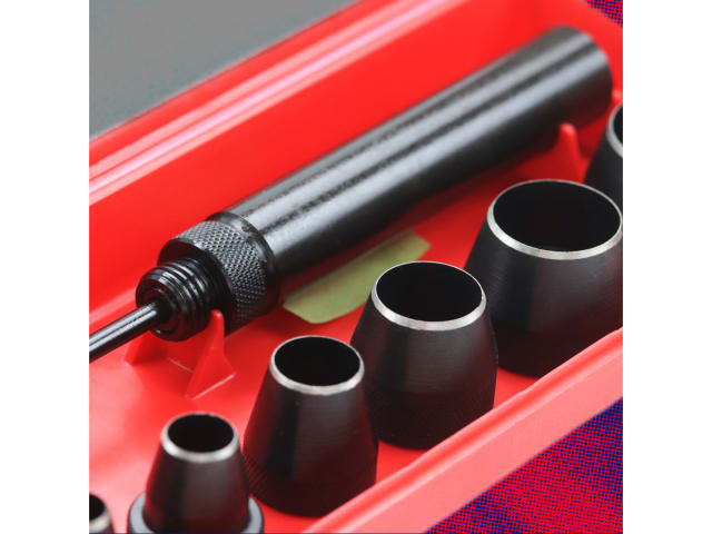 Black metal tool with various attachments on a red background
