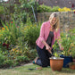 Woman gardening in a lush garden with various plants and tools.