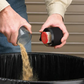 Person pouring sand from a container into a black trash bin.