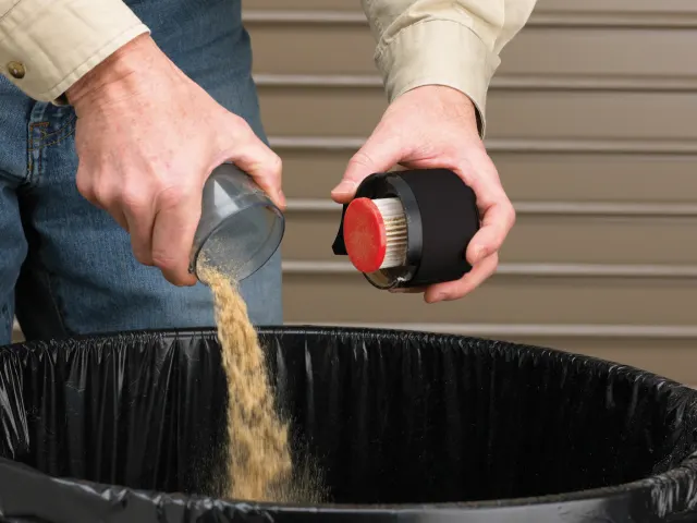 Person pouring sand from a container into a black trash bin.
