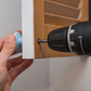 Person using a drill to attach a piece of wood to a wall.