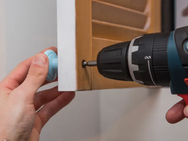 Person using a drill to attach a piece of wood to a wall.