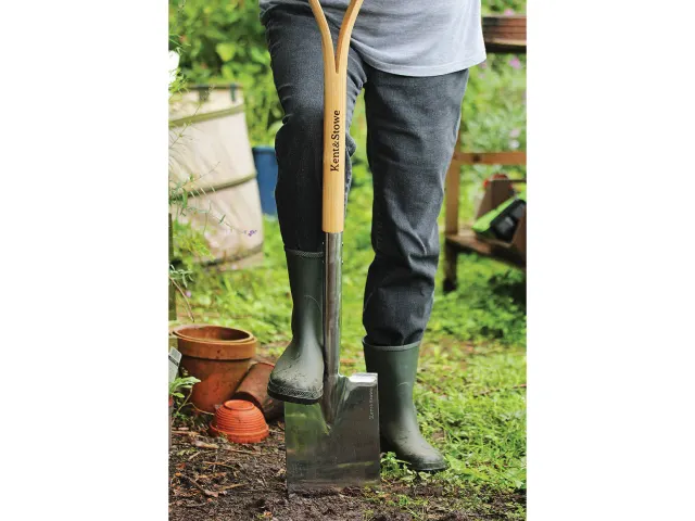 Person wearing green wellington boots holding a shovel in a garden setting