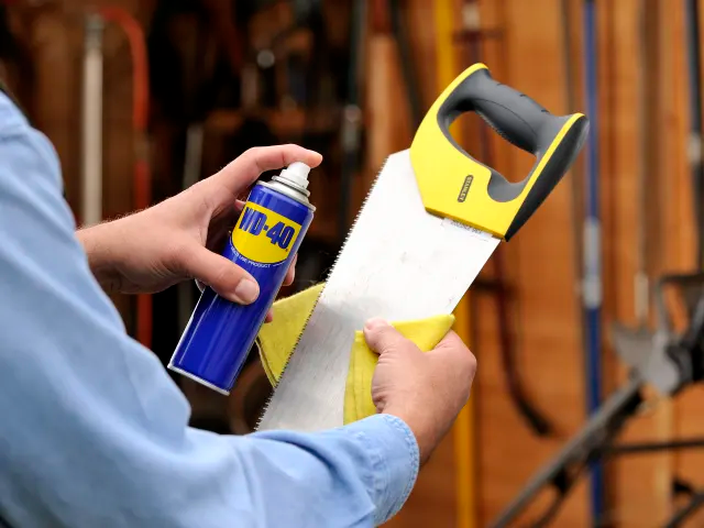 Person holding a saw and WD-40 spray can in a workshop setting