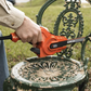 Person using a power tool on an ornate green chair outdoors.