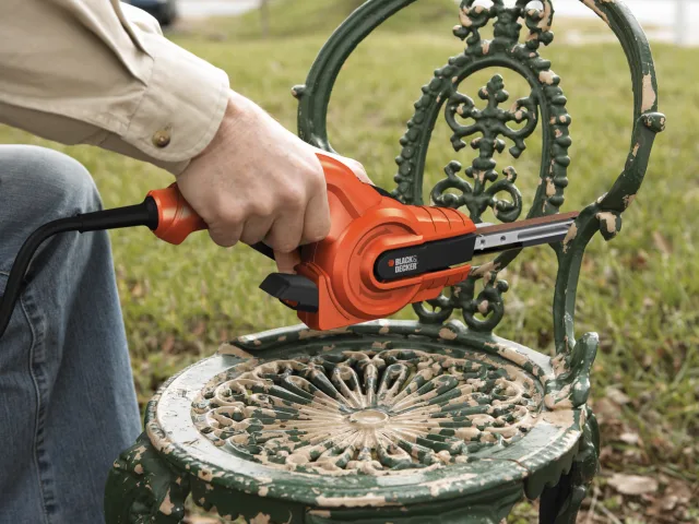 Person using a power tool on an ornate green chair outdoors.