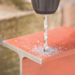 Drill bit drilling into a concrete block with a blurred outdoor background