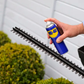 Person using a spray can to clean a hedge trimmer against a white wall.