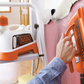 Person holding a Black+Decker handheld sprayer with a step stool and cleaning supplies in the background.
