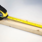 Tape measure being used to measure a wooden plank on a white background