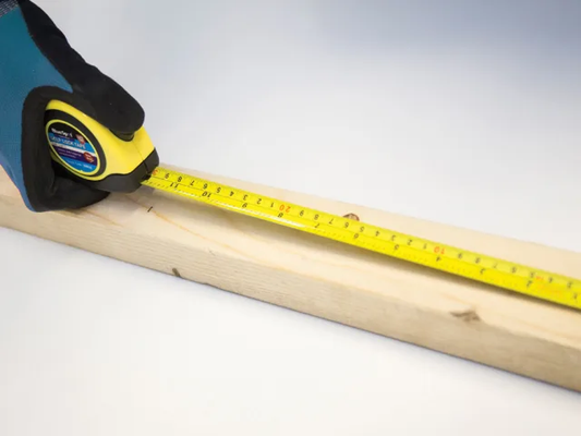 Tape measure being used to measure a wooden plank on a white background