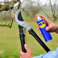 Person using a can of WD-40 on garden shears with a blurred natural background