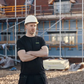 Man wearing a hard hat and black shirt standing in front of a construction site.