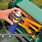 Hand holding a WD-40 spray can near a lawn mower on grass.