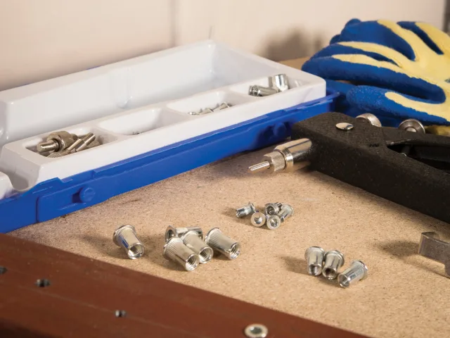 Tools and hardware on a workbench with a toolbox and gloves in the background.
