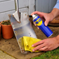 Person cleaning a metal shovel with a yellow cloth and WAG brand spray can outdoors.